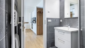 A modern bathroom with a white sink, dark tiles, and a wooden door leading to a kitchen.