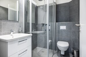 Un bany modern amb dutxa d'estuc de vidre, un lavabo blanc i un vàter.