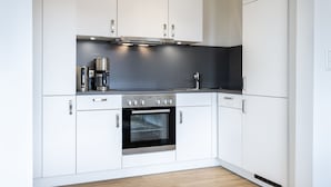 A modern kitchen with white cabinets, a built-in oven, and a coffee maker.