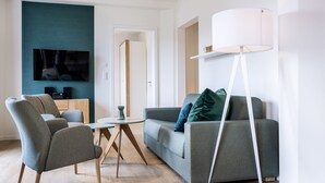 A modern living room with a grey sofa, two armchairs, a coffee table, a flat-screen TV, and a floor lamp.