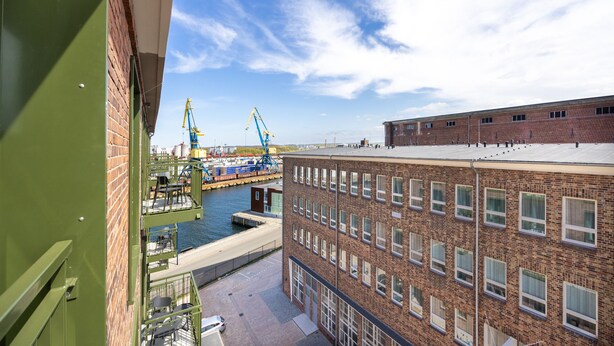 A view of a building with a brick facade and a flat roof overlooking a water body with cranes.