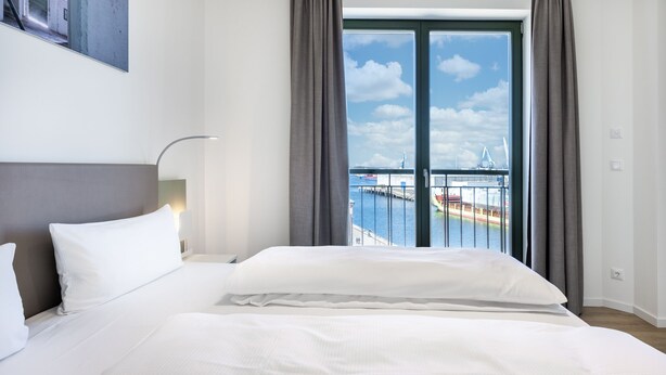 A hotel room with a large bed, a view of the sea, and a balcony with a railing.