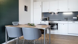 A modern kitchen with white cabinets, a stainless steel oven, and a wooden dining table with two grey chairs.