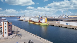 A harbor with a large cargo ship docked, a crane, and industrial buildings.