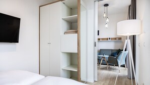 Una habitación de hotel moderna con una cama, un armario, una zona de estar con sofá y sillones, y un televisor montado en la pared.