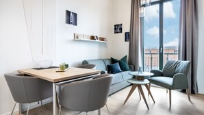 Una sala de estar moderna con un sofá, dos sillones, una mesa de comedor con sillas, una mesita redonda y un ventanal con cortinas.