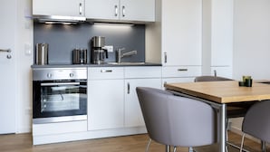 A modern kitchen with white cabinets, stainless steel appliances, and a wooden dining table.