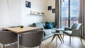 A modern living room with a sofa, chairs, a dining table, and a view of a building through a large window.