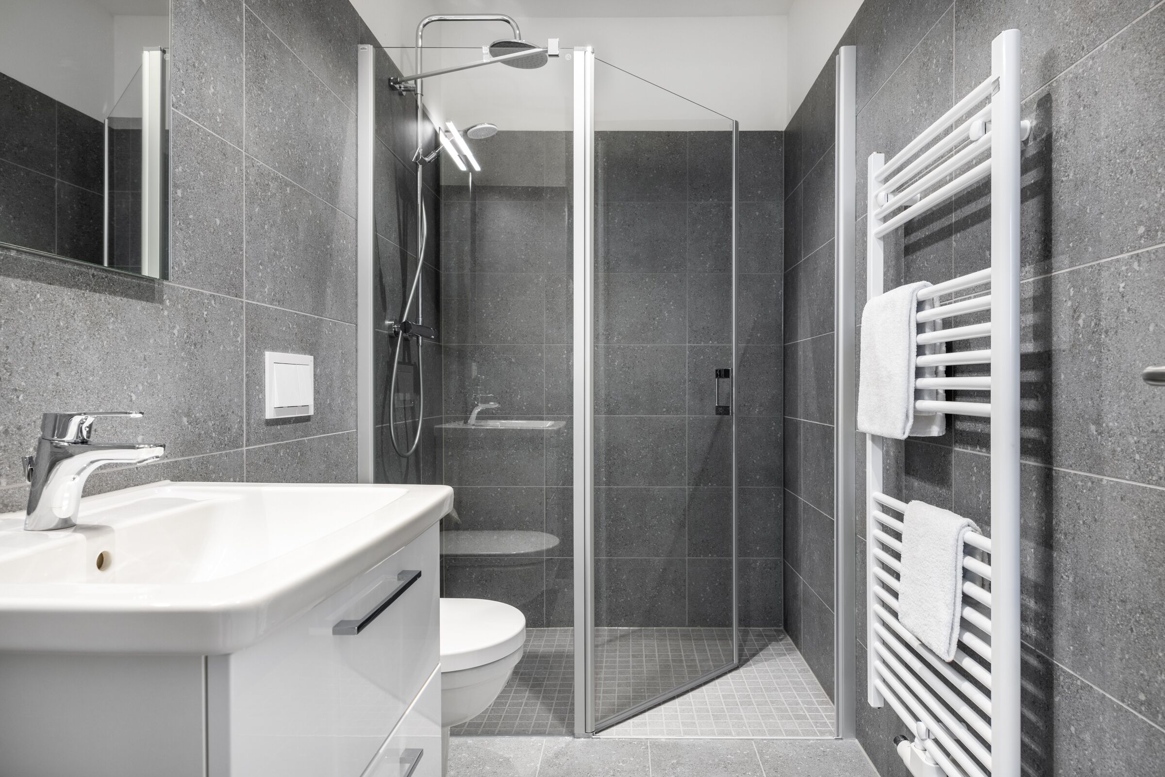 A modern bathroom with a glass-enclosed shower, a white sink, and a towel rack.