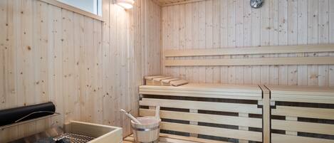 Uma sauna com bancos de madeira, um balde e uma grelha.