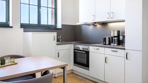 Una cocina moderna con armarios blancos, horno empotrado y cafetera sobre la encimera.