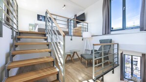 Un interior moderno con una escalera de madera, una zona de estar con una mesa y un gran ventanal con vistas.