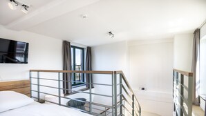 Habitación de hotel moderna con cama, televisor, ventana con cortinas, escalera y zona de ducha.