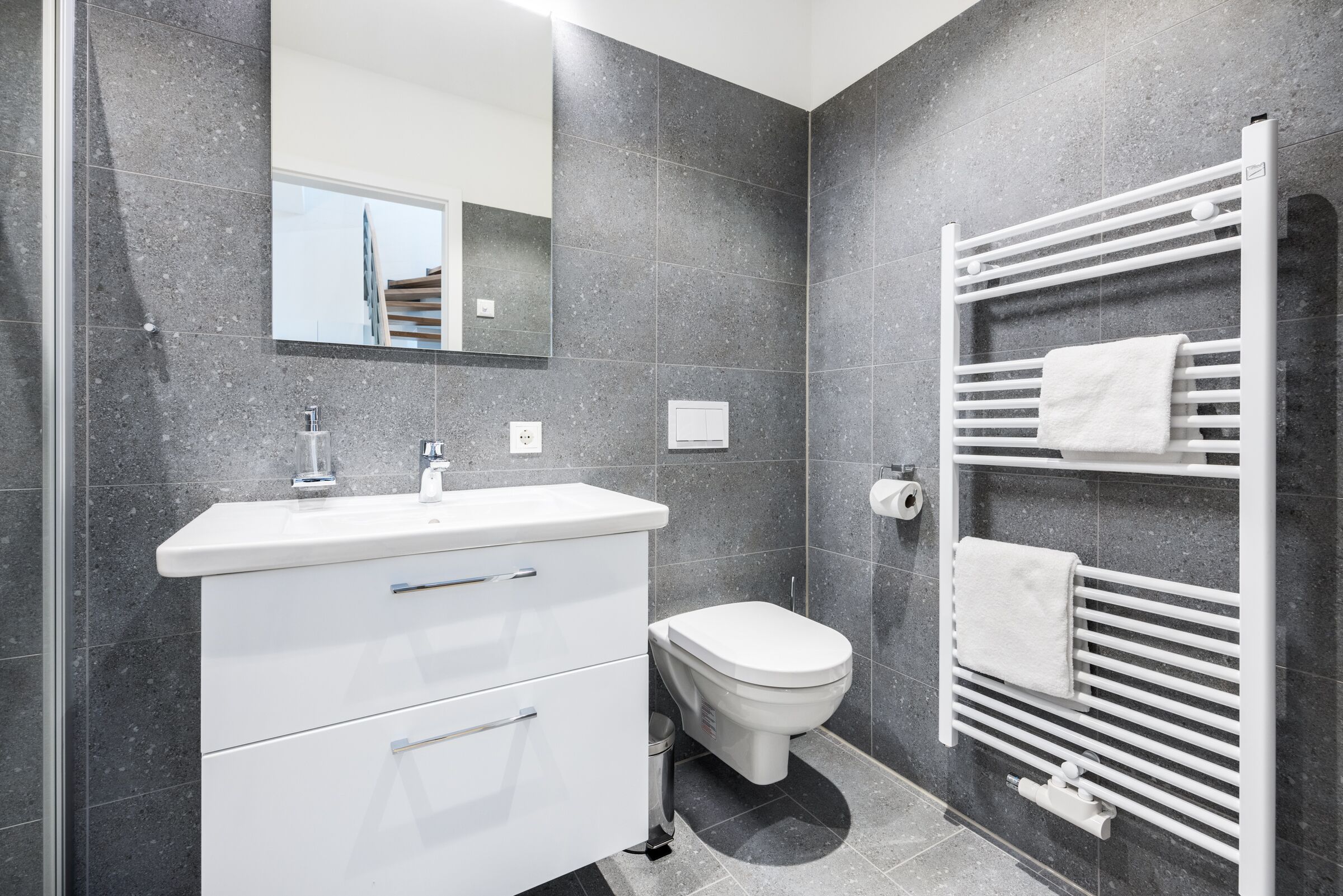 A modern bathroom with a white vanity, a toilet, and a towel rack.
