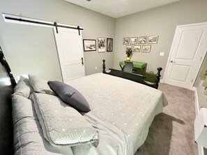 Cozy retreat with a neatly made bed, framed artwork, and a compact workspace.