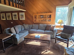 A living room with a sectional sofa, a coffee table, a wooden cabinet with decorative items, and framed pictures on the wall.