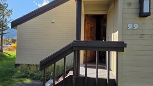 A building with a wooden door, a number '99' on the wall, and a small porch with a railing. - Snowcreek Resort Vacation Rental 99 (Mammoth Lakes)