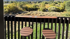 A balcony with two wooden stools and a table, overlooking a mountainous landscape. - Snowcreek Resort Vacation Rental 99 (Mammoth Lakes)