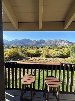 A balcony with two wooden stools and a table, overlooking a mountainous landscape.