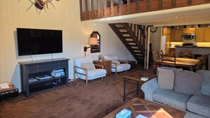 A living room with a TV, sofas, a coffee table, a staircase, and a kitchen area. - Snowcreek Resort Vacation Rental 99 (Mammoth Lakes)