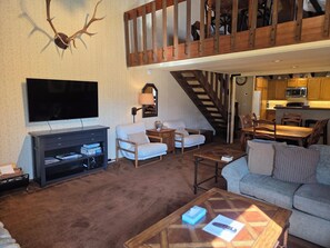 A living room with a TV, sofas, a coffee table, a staircase, and a kitchen area. - Snowcreek Resort Vacation Rental 99 (Mammoth Lakes)