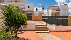 A residential building with a modern design, featuring a staircase leading to a gated entrance, surrounded by a well-maintained garden with palm trees and purple flowers. - Solis Villa, Albufeira, Algarve (Albufeira)