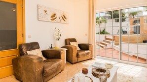 A living room with two leather sofas, a coffee table with decorative items, a vase with flowers, and a large sliding glass door leading to an outdoor area with steps and greenery. - Solis Villa, Albufeira, Algarve (Albufeira)