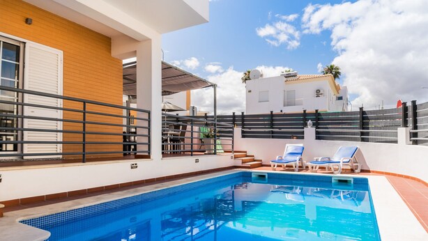 A swimming pool with lounge chairs, a wooden wall, and a white building in the background. - Solis Villa, Albufeira, Algarve (Albufeira)