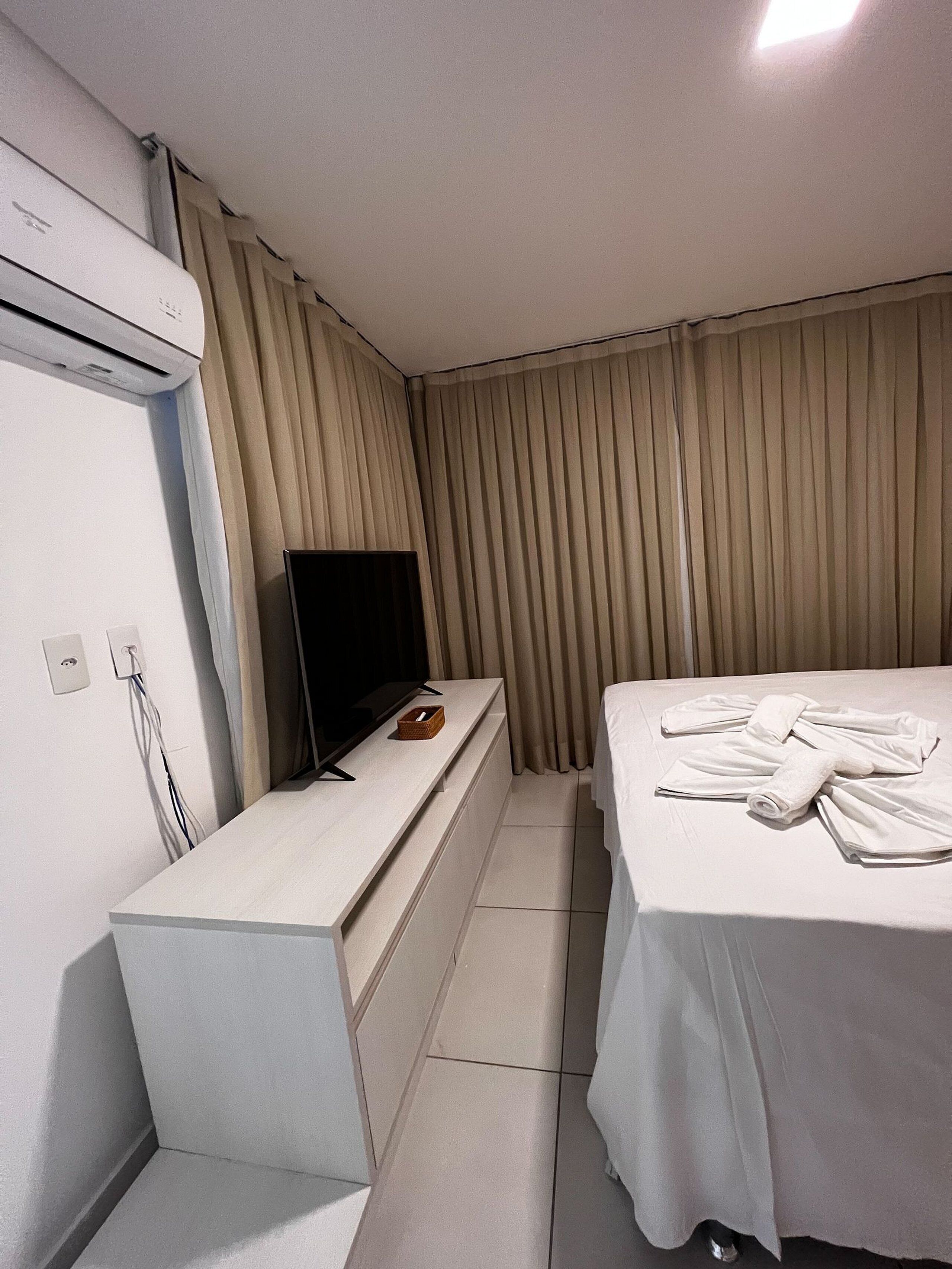 Ein Hotelzimmer mit einem Bett, einem Fernseher auf einem Schrank, einem kleinen Tisch und einer Klimaanlage.