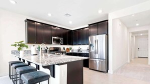 Una cocina moderna con armarios oscuros, electrodomésticos de acero inoxidable, una encimera de mármol y taburetes de bar.