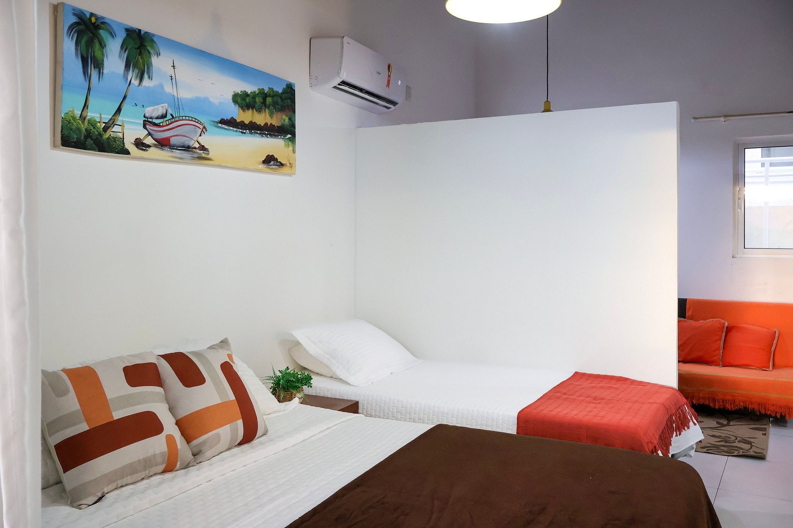 Una habitación con una cama, un sofá, un cuadro de un barco en la playa y un aire acondicionado.