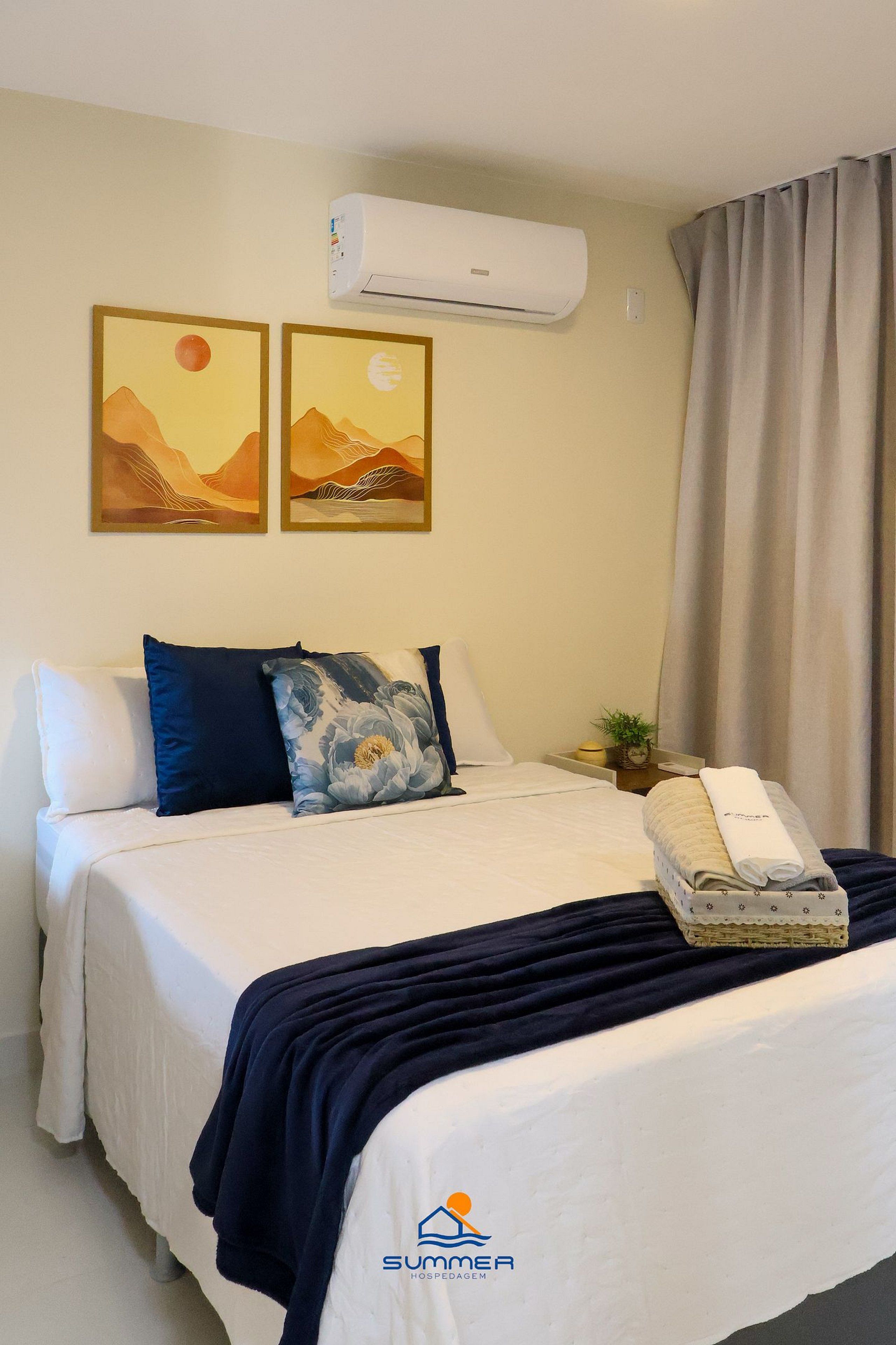 A hotel room with a bed, a nightstand with a lamp, a plant, and artwork on the wall.