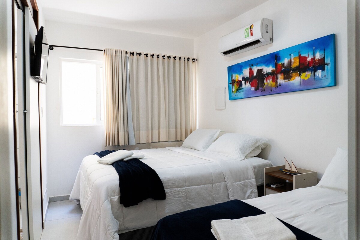 A hotel room with two beds, a painting, an air conditioner, and a window with curtains.