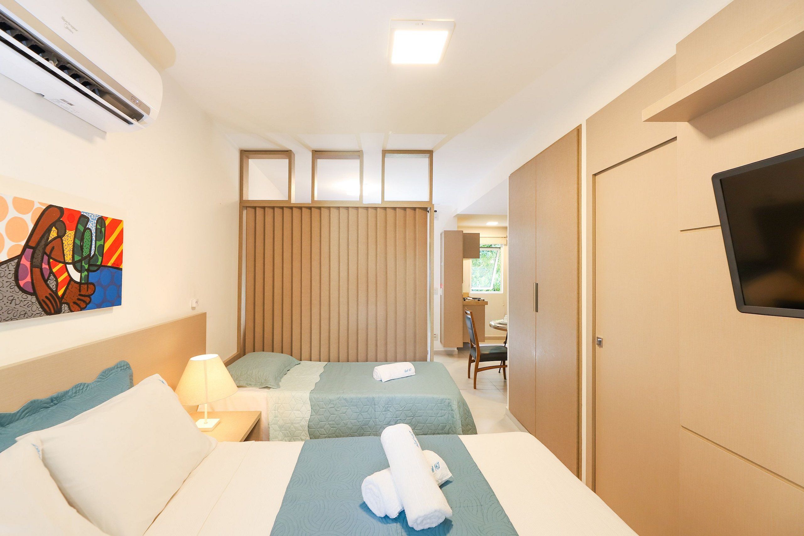 Ein Hotelzimmer mit zwei Betten, einem Fernseher, einer Klimaanlage und einem Bild an der Wand.