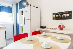 A compact kitchen with a refrigerator, a dining table with placemats, and a wall-mounted beer chart. - Solar Água Pipa- Summer Pipa (Tibau do Sul)