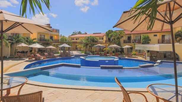 A swimming pool with lounge chairs and umbrellas, surrounded by buildings with balconies. - Solar Água Pipa- Summer Pipa (Tibau do Sul)