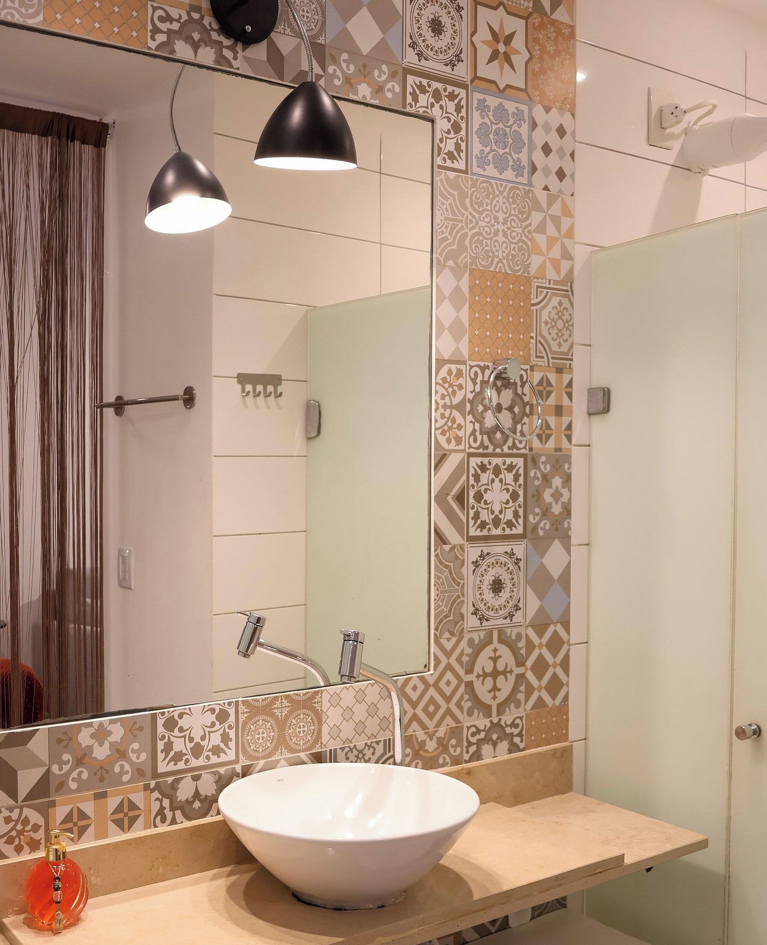 A bathroom with a white sink, two pendant lights, a shower, and patterned tiles.