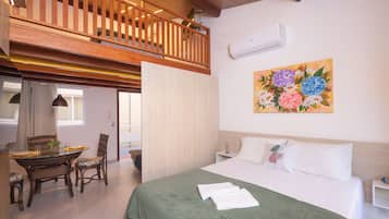 A bedroom with a bed, a dining table with chairs, a balcony, and a painting on the wall.