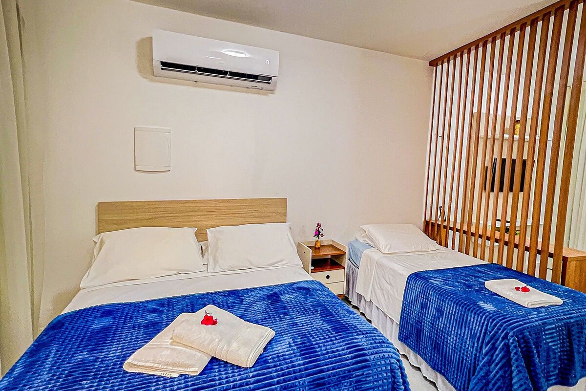 Two beds with blue bedding, a ceiling light, an air conditioning unit, and a wooden slat partition.