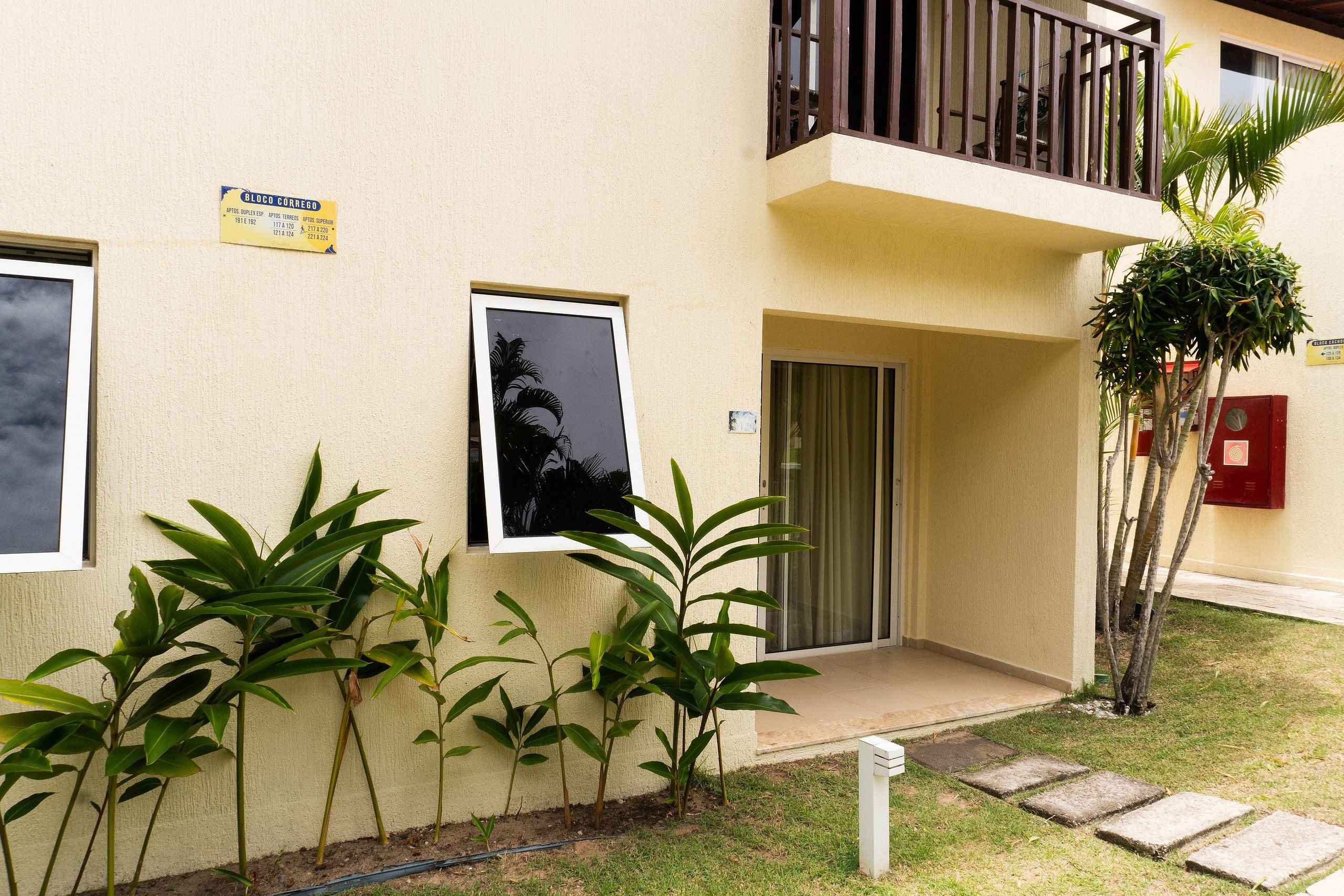 A building with a balcony, a door, and a small garden with plants.