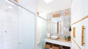 Ein Badezimmer mit Duschabtrennung aus Glas, einem weißen Waschbecken mit Aufsatzbecken, einer gemusterten Rückwand und Wickerkörben unter dem Waschbecken.