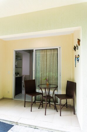 A balcony with wicker furniture, a glass door, and a small table with a vase. - Solar Água Pipa- Summer Pipa (Tibau do Sul)