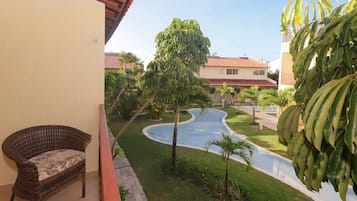 A balcony with a wicker chair, a swimming pool, and surrounding greenery.