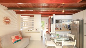 A modern kitchen with a refrigerator, microwave, and dining area with chairs and a glass table. - Solar Água Pipa- Summer Pipa (Tibau do Sul)