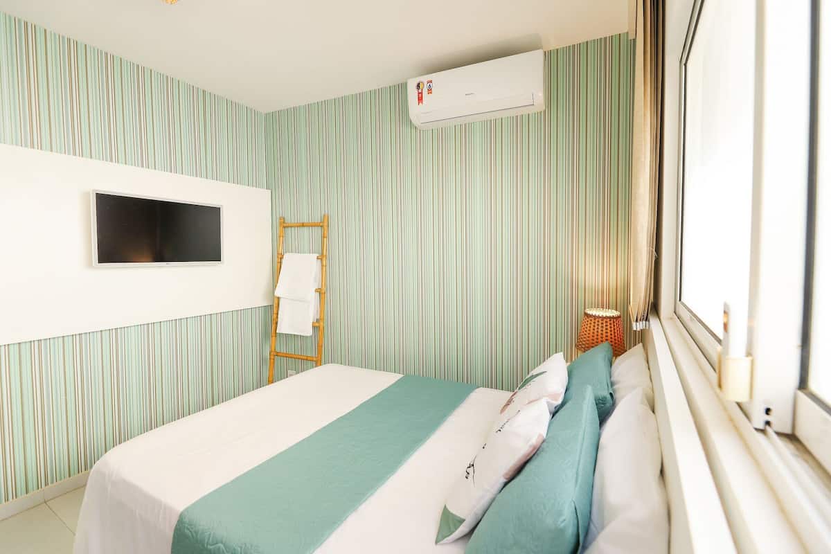 Una habitación de hotel con cama, televisión de pantalla plana, aire acondicionado, ventana con vistas y pared a rayas.