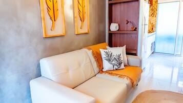 A modern living room with a white leather sofa, a decorative pillow, and two wall-mounted leaf paintings.