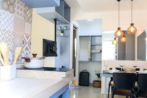 A modern kitchen with a stove, pots, and wooden utensils. There are hanging lights, a dining table with chairs, and a basket. - Solar Água Pipa- Summer Pipa (Tibau do Sul)