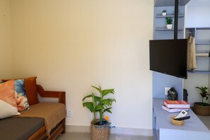 A modern living space with a sofa, a flat-screen TV, a small plant, and a basket with a remote control. - Solar Água Pipa- Summer Pipa (Tibau do Sul)