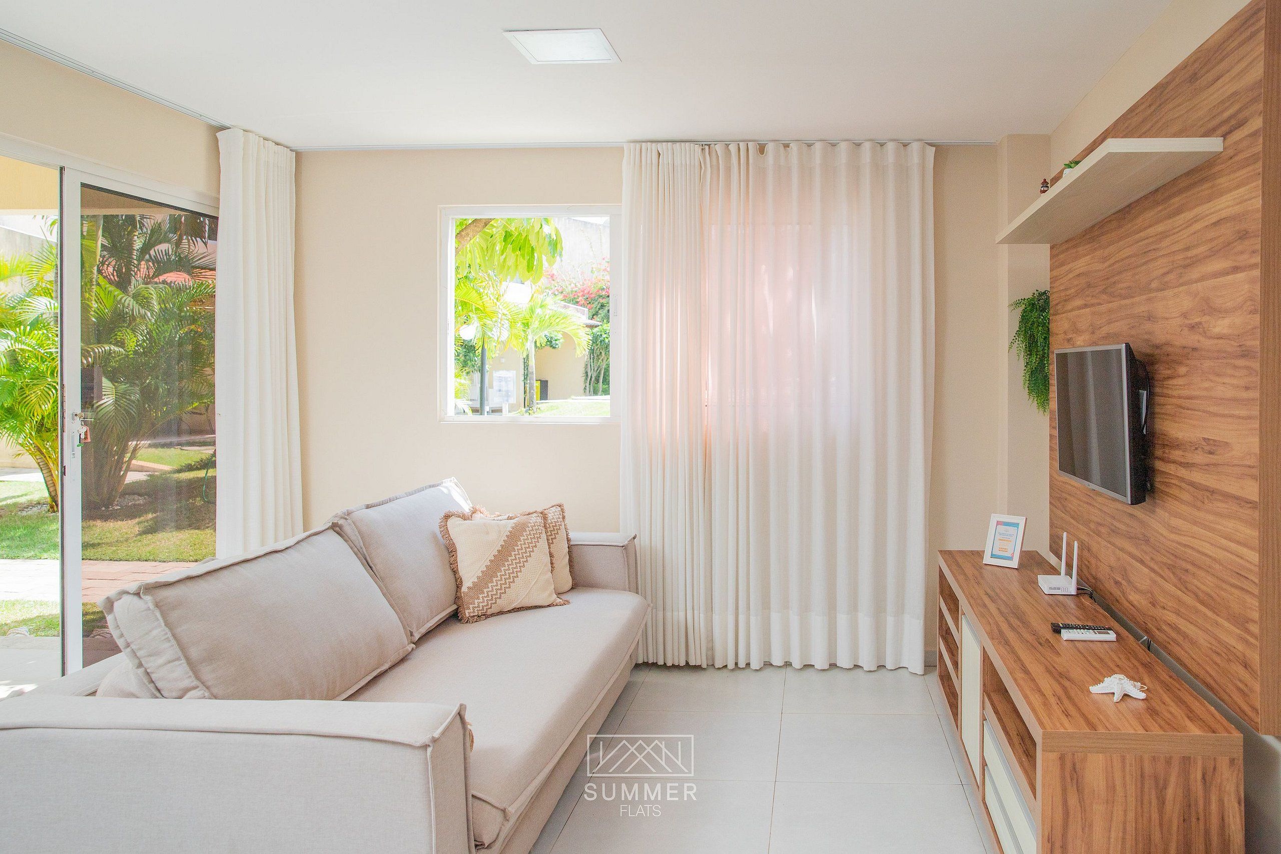 Una sala moderna con un sofá, cortinas, un televisor y un mueble de madera.
