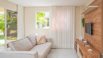 Una sala moderna con un sofá, cortinas, un televisor y un mueble de madera.